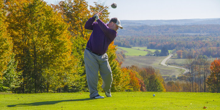 Man golfing overlooking valley with colorful fall foliage all around