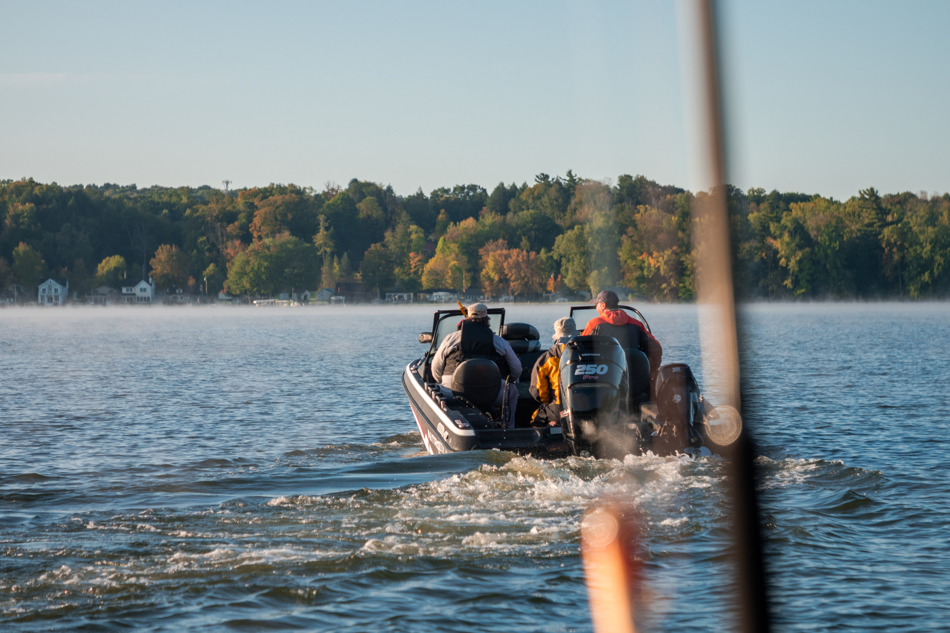 Three anglers on a fishing boat on Chautauqua Lake. Tree foliage is fall colors