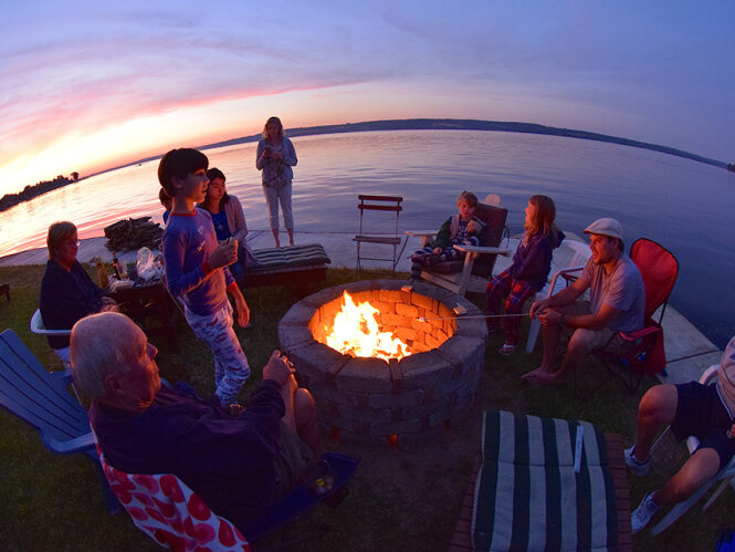people gathered around a campfire at sunset near a lake